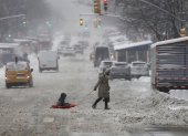 Una mujer y un niño sobre un trineo fueron registrados este sábado al cruzar una calle cubierta de nieve en Nueva York (NY, EE.UU.).