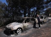 Una mujer observa los coches quemados del incendio acaecido en Anthousa, cerca de Atenas, Grecia.