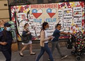 Varias personas caminan frente a una pared con información relacionada al plebiscito constitucional en Santiago (Chile).