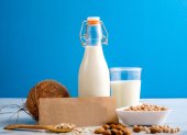 Lactose free milk. Bottle and glass of milk, almond nuts, oat flakes, coconut and piece of paper with text LACTOSE FREE on wooden surface on blue background. Lactose intolerance food concept