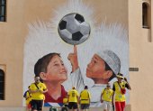 Un grupo de hinchas ecuatorianos reunidos en Qatar con una imagen alegórica al Mundial en un muro.