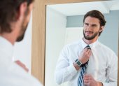 Man getting dressed in bedroom while looking at mirror at home