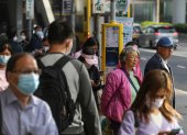 Viajeros, algunos de ellos todavía con mascarillas, esperan en una parada de autobús en Hong Kong, China, 01 de marzo de 2023