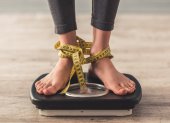 Cropped image of woman feet standing on weigh scales, on gray background. Legs winded with a tape measure