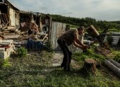 Mykola (R), de 58 años, corta leña mientras su madre Nina, de 92, se sienta en su patio entre los restos de su casa en el pueblo de Bohorodychne, región de Donetsk, Ucrania