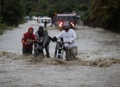 SAN JOSÉ DE OCOA (REPÚBLICA DOMINICANA), 04/10/2023.- Personas cruzan con dificultad la carretera que se encuentra inundada producto de las intensas lluvias, hoy en San José de Ocoa (República Dominicana). Una persona está desaparecida, al menos 1.522 fueron desplazadas de sus hogares y un puente colapsó debido a las intensas lluvias en la República Dominicana, que han llevado a las autoridades a decretar la alerta en 30 de las 32 provincias del país, 11 en nivel rojo. EFE/Orlando Barría