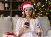 Worried concerned girl in Christmas Santa hat having problems with payment by credit card online for New Year purchases, looking at smartphone screen with puzzled face. Scam, fraud concept