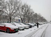 Un hombre transita por una calle en donde los carros aparecen estacionados y cubiertos bajo un manto blanco y congelado, en Pekín, este miércoles 13 de diciembre de 2023.
