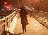 Una mujer al caminar con dificultad sobre un puente peatonal elevado y bajo una fuerte torementa de nieve en Shanghái (China).