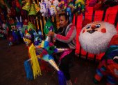 Tradición. Una vendedora sostiene una piñata en el mercado de Jamaica, en Ciudad de México y habla sobre las ventas de los productos.