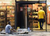 Desigualdades. Una persona en condición de calle espera ayuda de transeúntes afuera de un minimercado.