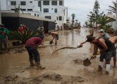 Personas ayudan a remover el lodo en una calle afectada por las lluvias, en Lima (Perú).