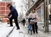 La gente espera un autobús en la calle después de una Nevada en Beijing, China, 21 de febrero de 2024.