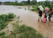 personas cruzan con sus pertenencias por un río en medio de las inundaciones causadas por la tormenta tropical Sara en El Progreso, Honduras.