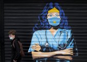 Un chico con mascarilla pasa delante de un mural en Pristina (Kosovo)