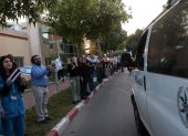 Personas y personal del Centro Médico Shamir frente al complejo hospitalario de Beer Yaakov, ondean banderas mientras llegan ambulancias de la policía que transportan a cinco rehenes recién liberados.