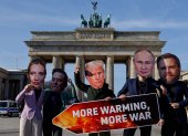 Activistas con máscaras de líderes del mundo sostienen un cartel que dice "Más calentamiento, más guerra".