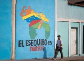 Transeúntes caminando frente a un mural con el mapa de Venezuela que dice "El Esequibo es nuestro", en Caracas.