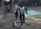 Un técnico camina detrás de un robot humanoide antes de la carrera de humanos y robots en Pekín.