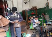 Oswaldo Cujilema (de pie) cose la planta de una zapatilla en su local “Cosedora Los Andes”, donde continúa el legado de su abuelo zapatero.