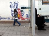Una mujer iraní con velo se sienta en una estación de autobuses junto a un mural antiestadounidense cerca de la antigua embajada de Estados Unidos en una calle de Teherán.