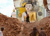 Fotografía del 12 de abril de 2025 muestra a un hombre retirando escombros alrededor de una dañada estatua de Buda