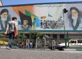 Iraníes caminan junto a una pintura mural del líder supremo iraní, el ayatolá Ali Jameneí (arriba-i) y el fallecido líder supremo iraní, el ayatolá Ruhollah Jomeiní (arriba-d), en una calle de Teherán.