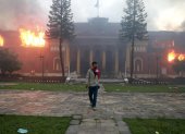 A man is draped in the Nepal national flag as a fire rages through the president"s office in Kathmandu on September 9, 2025, a day after a police crackdown on demonstrations over social media prohibitions and corruption by the government. Nepali youth protesters set fire to parliament on September 9 as the veteran prime minister obeyed furious crowds to quit, a day after one of the deadliest crackdowns in years in which at least 19 people were killed. (Photo by Anup OJHA / AFP)