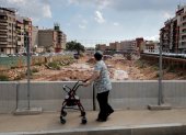 Restos. Una adulta mayor camina sobre un puente mientras trabajadores instalan estructuras y enormes piedras en el seco canal artificial de Paiporta.