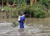 Fotografía del 29 de octubre de 2025 de un hombre cruzando un río crecido mientras carga a un niño, en el poblado de Guama en Santiago de Cuba (Cuba).