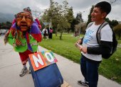 Una persona disfrazada sostiene una maleta mientras un hombre lo observa durante una manifestación contra el referéndum en Quito (Ecuador).