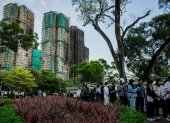 Varias personas dejan flores como tributo a las víctimas del incendio del complejo residencial Wang Fuk Court, en el fondo.