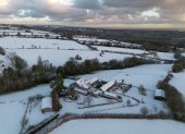 La imagen muestra un paisaje rural cubierto de nieve y edificios agrícolas en el Reino Unido durante una importante ola de frío a inicios de 2026.