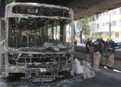 Bomberos observan los restos de un autobús incendiado por supuestos integrantes de una facción criminal, en respuesta a la muerte de Claudio Augusto dos Santos en Río de Janeiro