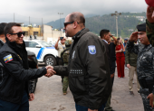 El presidente Daniel Noboa estrecha la mano del ministro del Interior, John Reimberg, durante un acto oficial acompañado por personal militar.