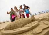 Un grupo de turistas se toma una foto frente a una escultura hecha con arena en una playa de Manabí.