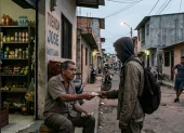 Un tendero local entrega dinero en efectivo a un joven enmascarado en una calle.