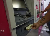 Personas usan los cajeros automáicos para retirar o depositar dinero.