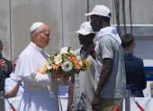 El papa León XIV recibe flores de dos voluntarios para protagonizar una ofrenda floral en el mar en recuerdo de los migrantes muertos.
