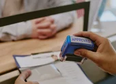 Referencial.Un funcionario estampa la aprobación en un trámite, mientras un solicitante espera la resolución en la oficina.