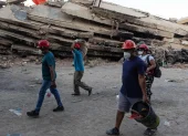 Personas caminan frente a los escombros de un edificio tras los sismos en La Guaira, Venezuela.