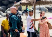 Un agente coordina con vecinos en la playa de Ceuta durante la llegada masiva de migrantes desde Marruecos.