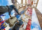 Dos personas hacen labor de mantenimiento en una torre donde se extrae petróleo.
