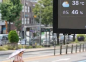 Un tablero digital muestra 38 °C en una calle de Pyongyang, mientras un transeúnte se protege del sol con sombrilla en plena ola de calor.