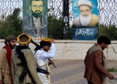 Personas armadas pasan junto a pinturas que representan a líderes hutíes fallecidos, expuestas en una valla en Saná, Yemen, el 7 de septiembre de 2026.