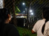 Unas mujeres miran a través de una valla durante una vigilia para exigir la liberación de los presos políticos venezolanos frente a la prisión El Rodeo I en Guatire.