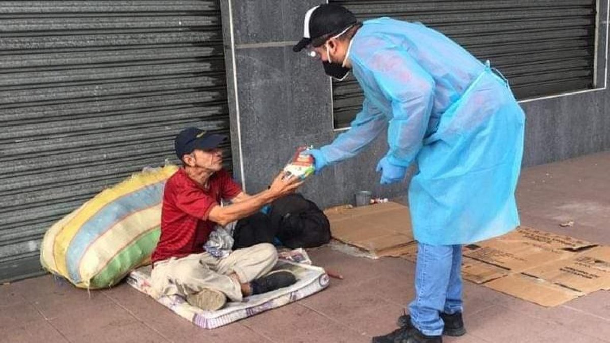 Un voluntario entrega comida a una persona que duerme en la calle.