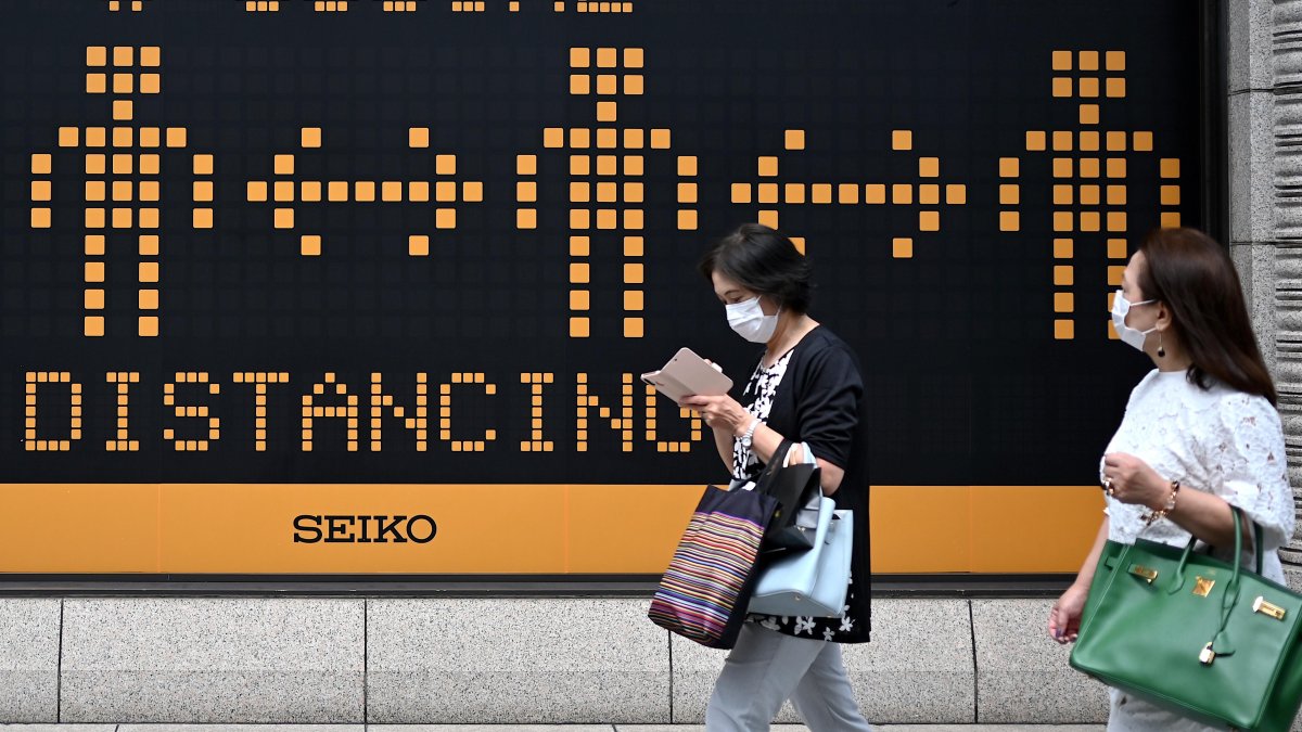En Tokio, peatones pasan junto a una valla publicitaria que recuerda a las personas las prácticas de distanciamiento social en medio de la pandemia, en junio pasado.