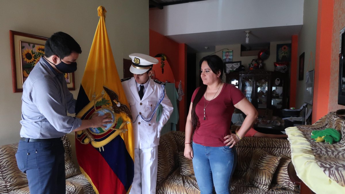 Anthony Santillán Mora, abanderado de la Academia Naval Guayaquil, recibe en su casa la bandera por parte de un directivo de la plantel. A su lado está su mamá.