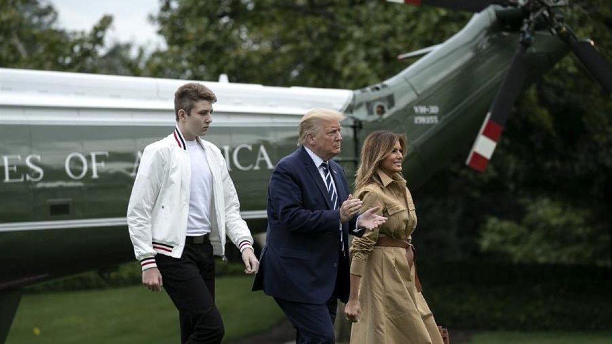 Barron Trump, de chaqueta blanca y pantalones negros, junto a sus padres Donald y Melania Trump.